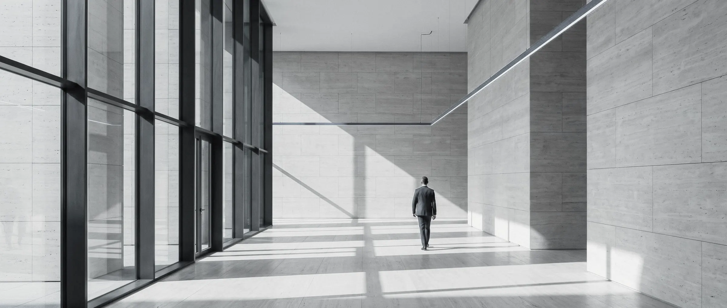 Un professionista attraversa un atrio contemporaneo in travertino e vetro, illuminato da una linea di luce.